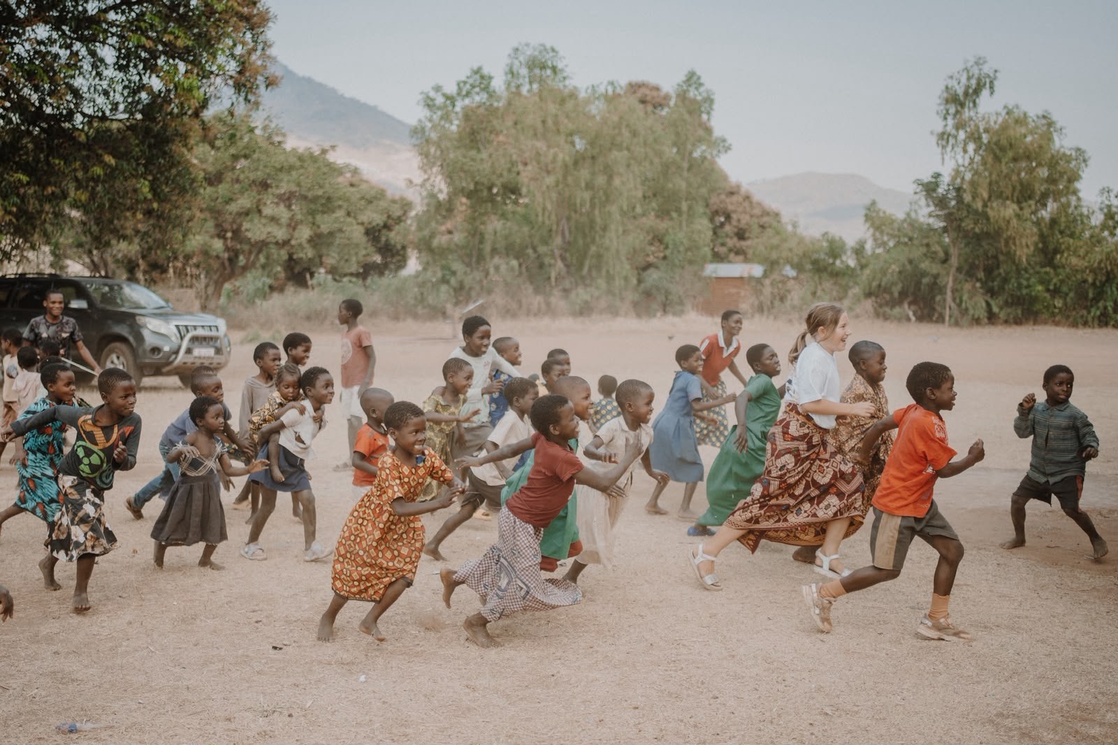 A team member praying in a circle with children, wearing a Go and make disciples shirt