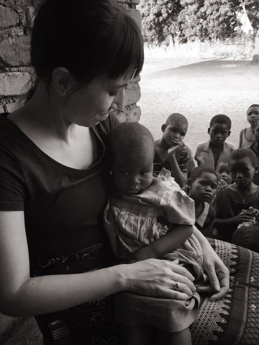 A team member holding a small child while village children look on