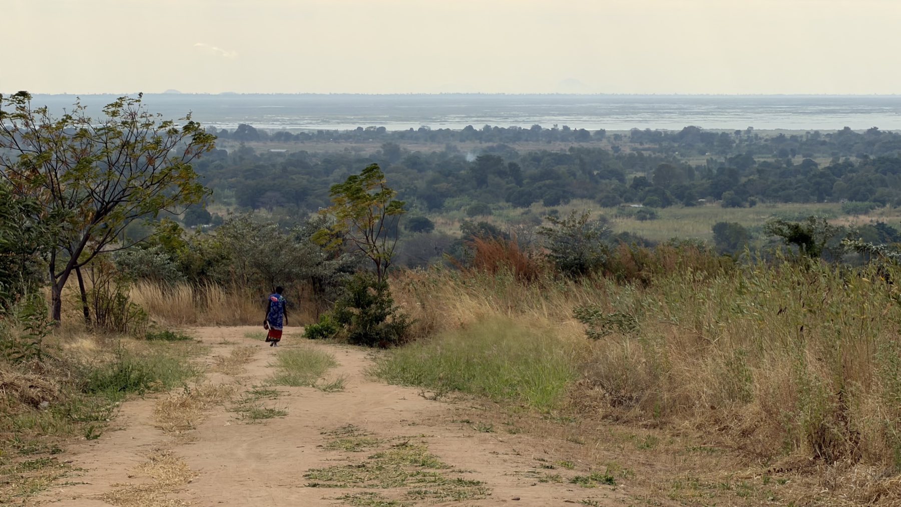 A woman walking a dirt road toward the lake in Malawi