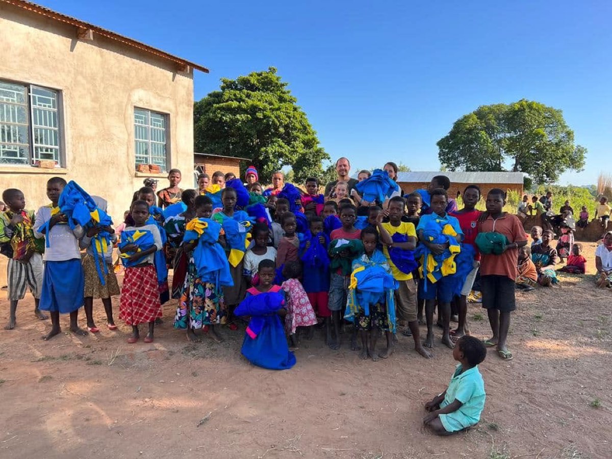 Children holding school supplies outside a village building