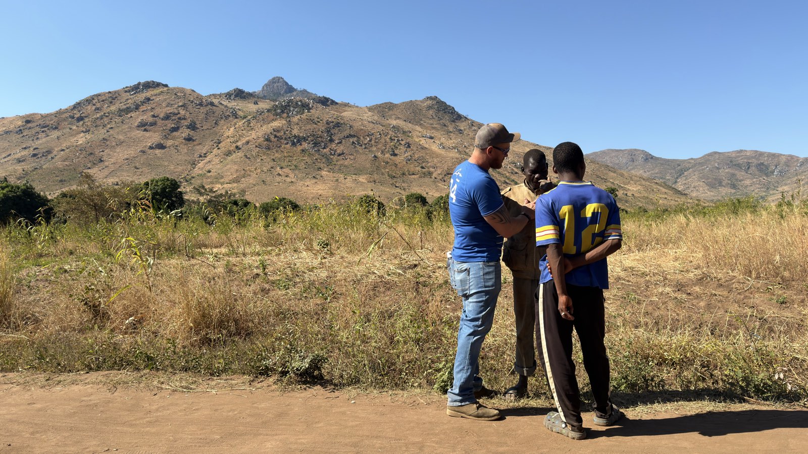 Praying with two young men on a dirt road below the mountains