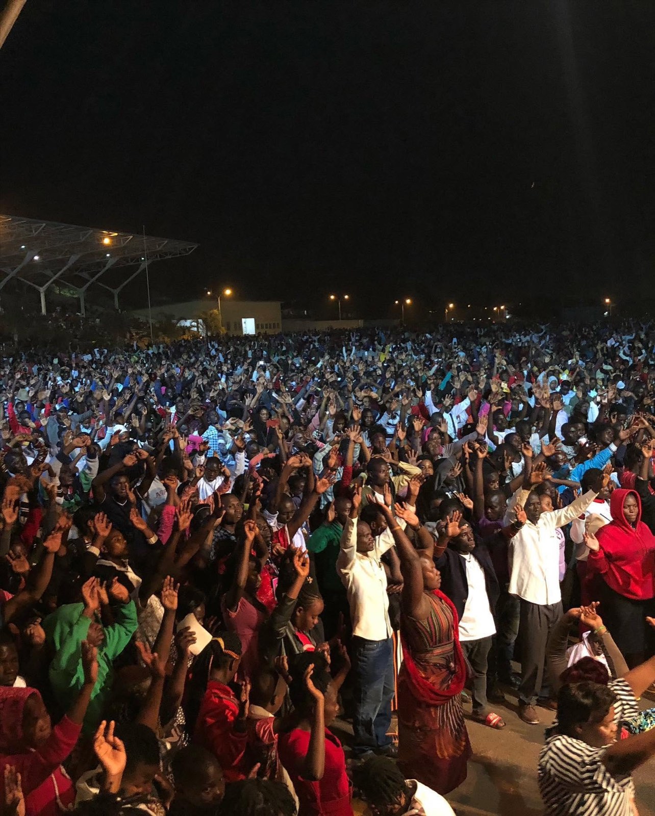 A large crowd with hands raised at an evening crusade