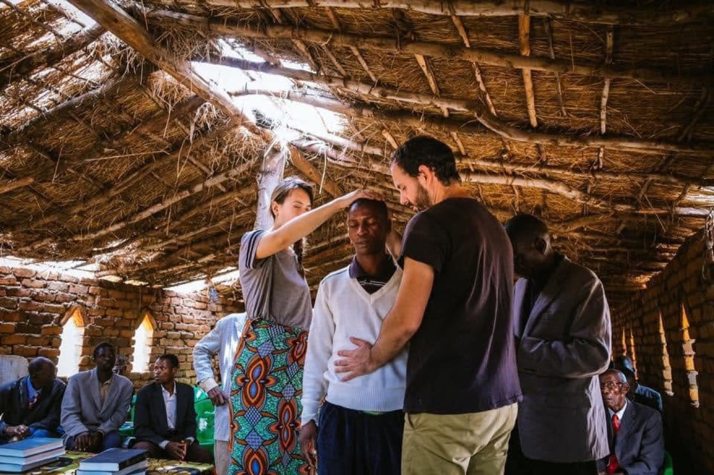 Praying over a man inside a grass-roofed village church