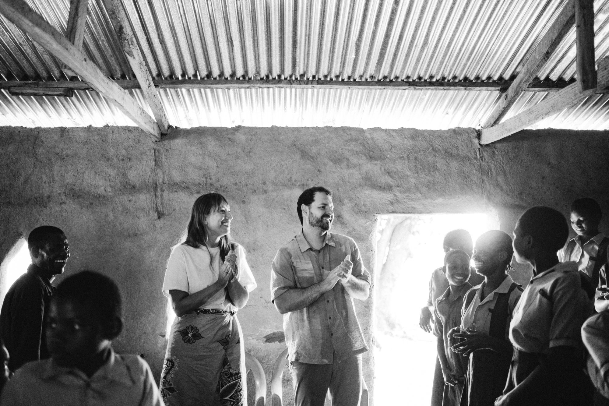 Two missionaries clapping and smiling with children inside a village schoolroom